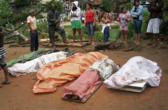 People stand by the bodies of mudslide victims after heavy rain in the neighborhood of Caleme in Teresopolis, Brazil on Wednesday. 